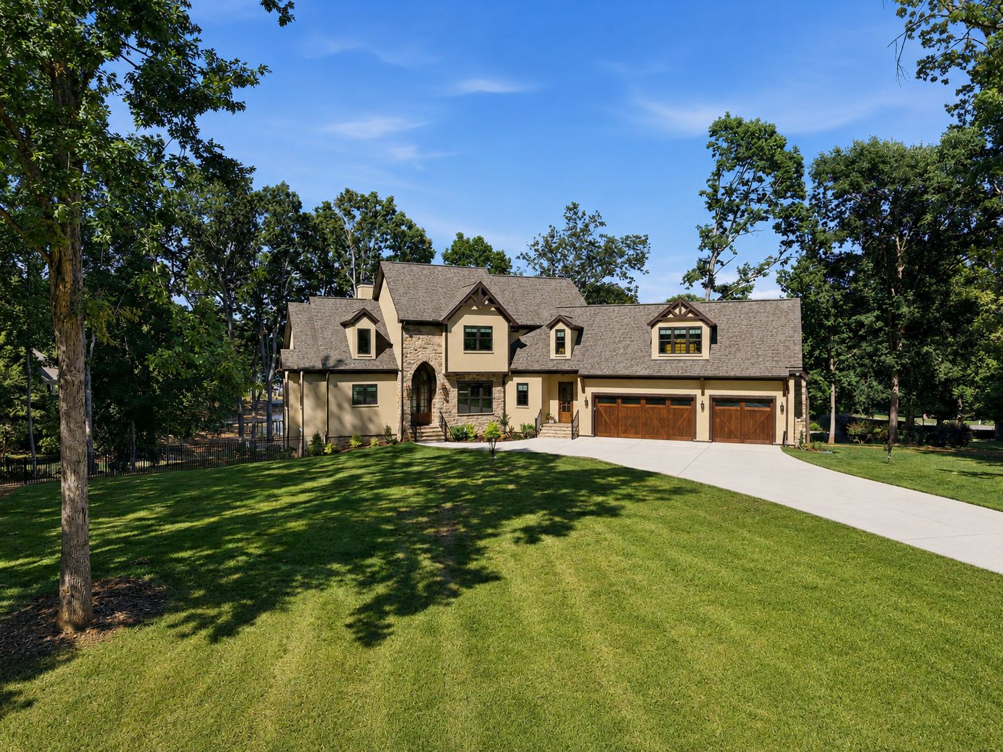 Front elevation: sand stucco and fieldstone, walnut-stained carriage doors, set on a broad lawn among mature hardwoods