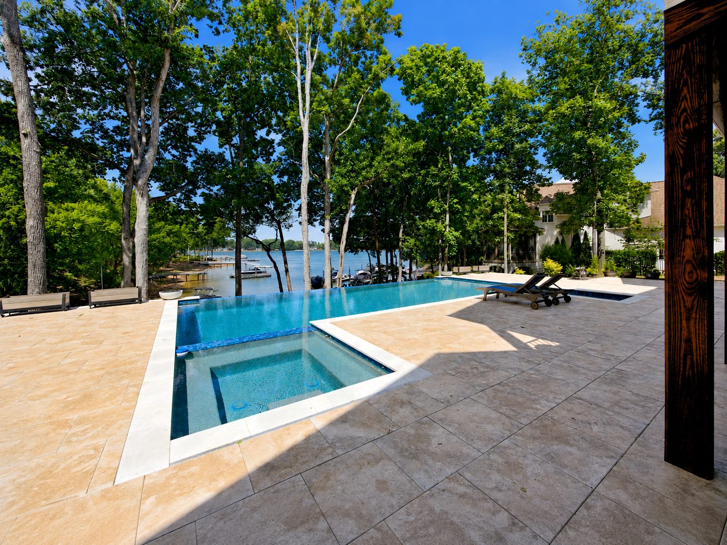 Infinity-edge pool and spa on a stone terrace, with docks on Lake Norman beyond the trees
